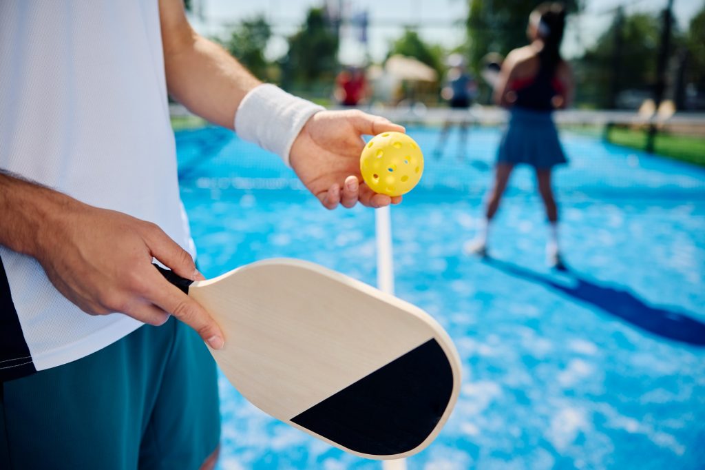 Close up of man serving the ball while playing mixed doubles in pickleball.